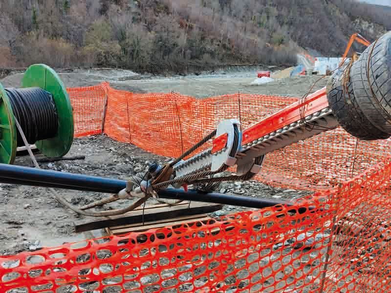 Cantiere con recinzione di sicurezza arancione, una perforatrice e bobine di cavi.