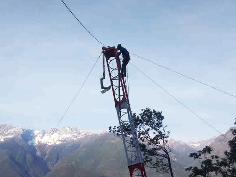 Uomo su un'alta torre di comunicazione, che ripara i cavi con uno sfondo montuoso.