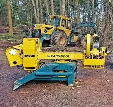 Macchina forestale SilvaTrade gialla e blu che taglia il legname, con un trattore giallo sullo sfondo in una foresta.