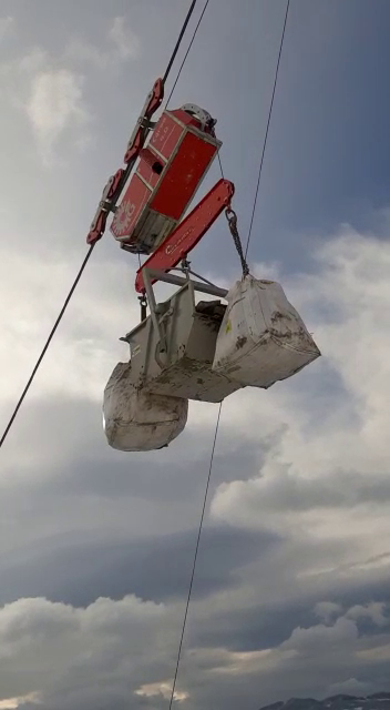 Sollevamento tramite secchio che trasporta sacchi contro un cielo nuvoloso.