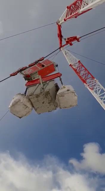 Una gru con braccio rosso e bianco che sostiene un peso è in equilibrio sullo sfondo di un cielo nuvoloso.