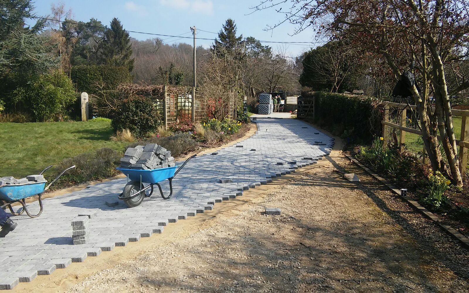 A blue wheelbarrow is sitting on a part-finished block paved driveway