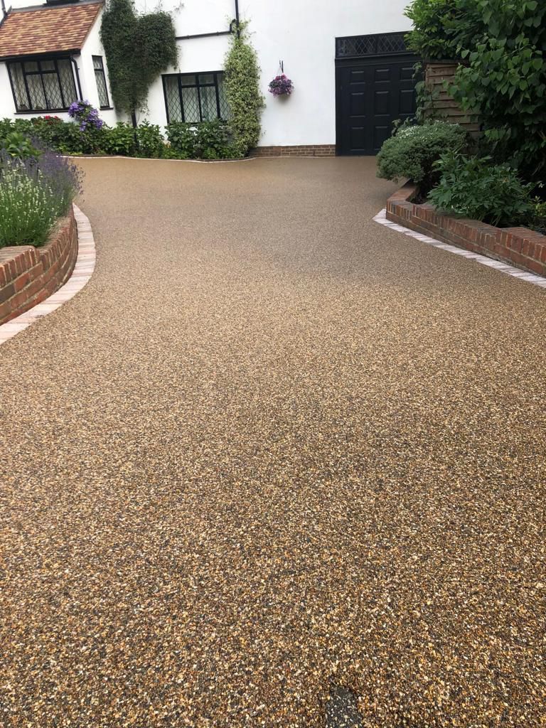 A gravel driveway leading to a house with a brick wall.