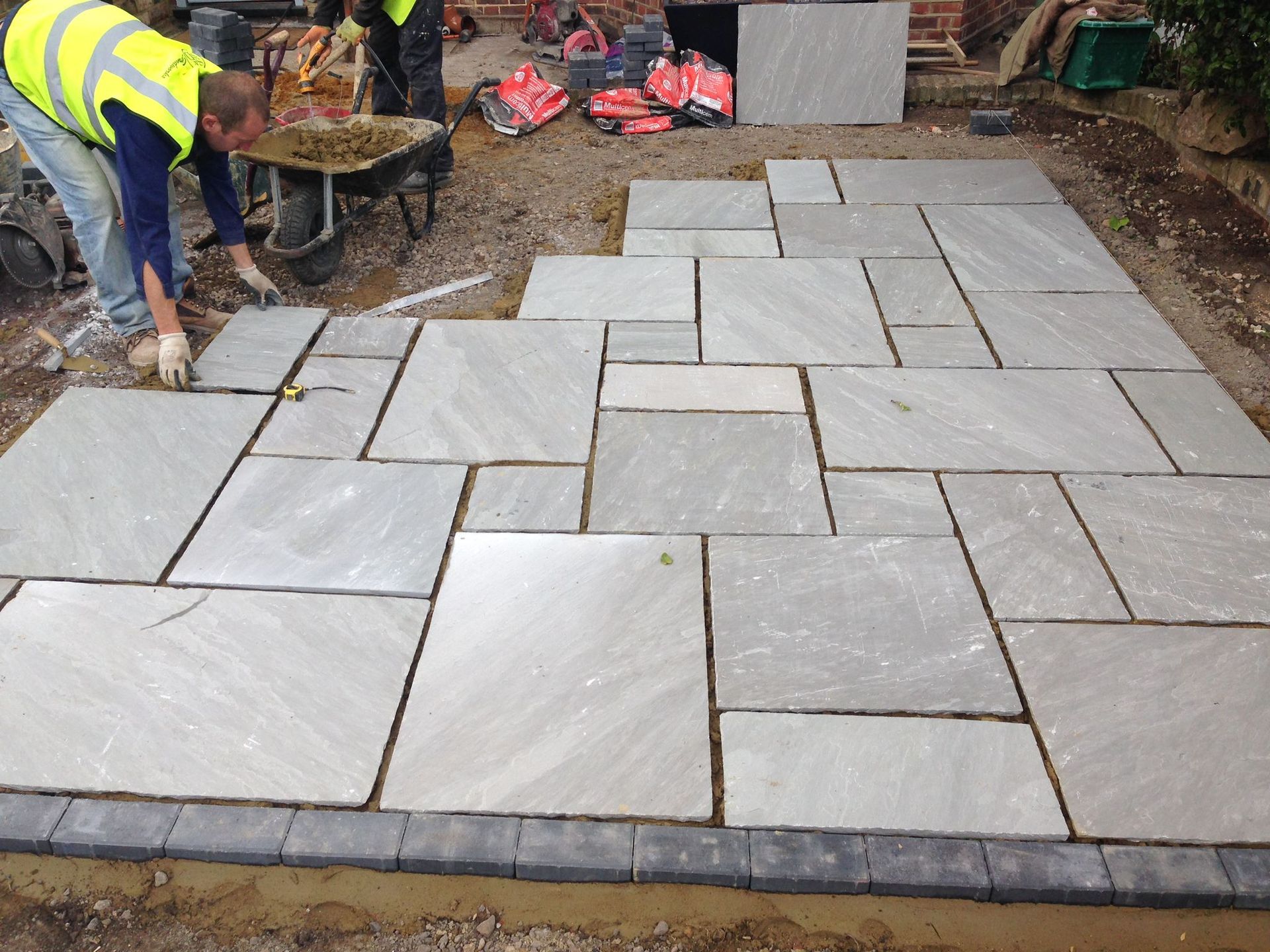 A man in a yellow vest is working on a tiled floor