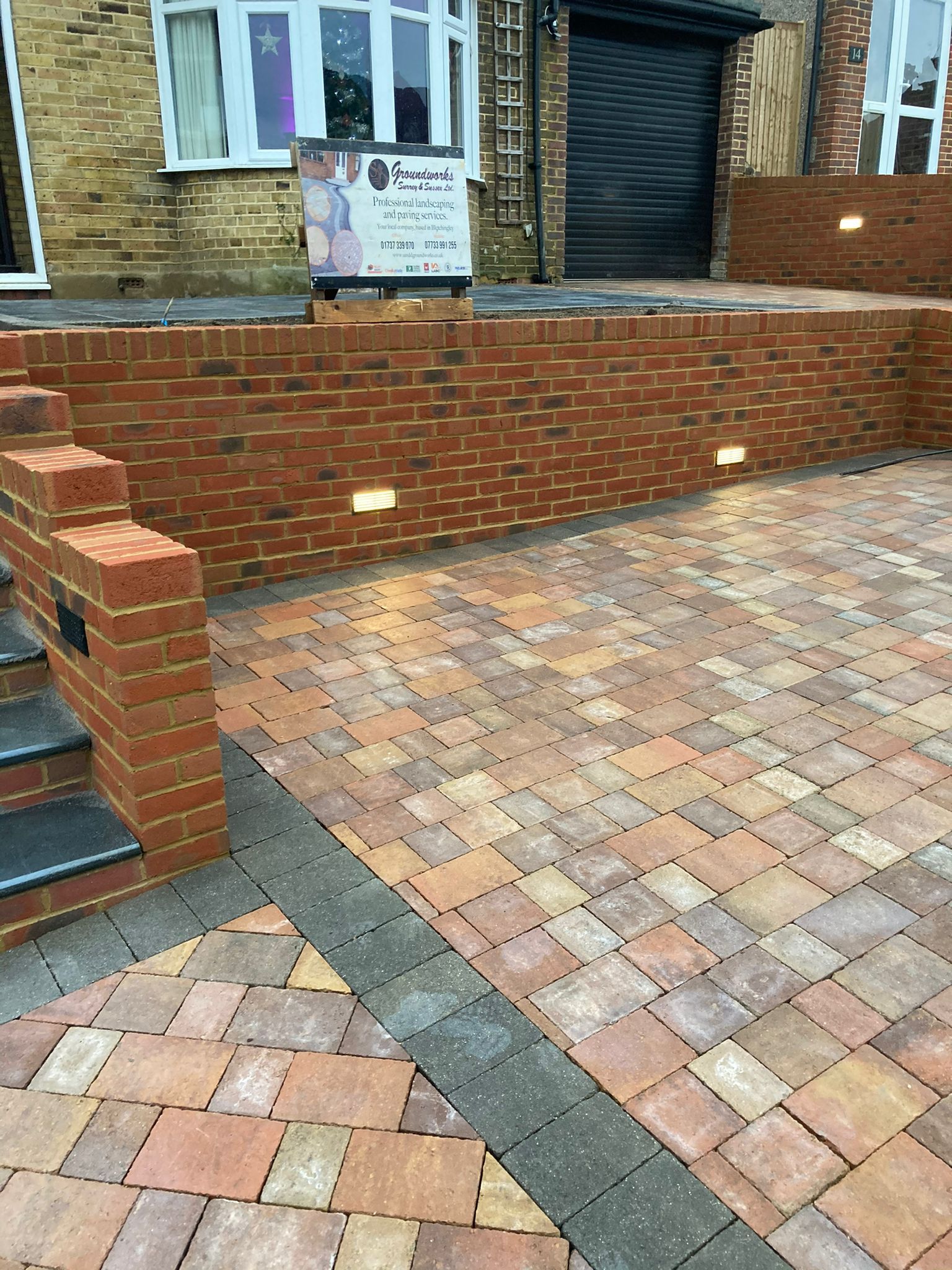 A brick driveway with stairs and a brick wall in front of a house.