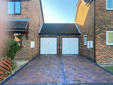 A driveway leading to a brick house with two garage doors.