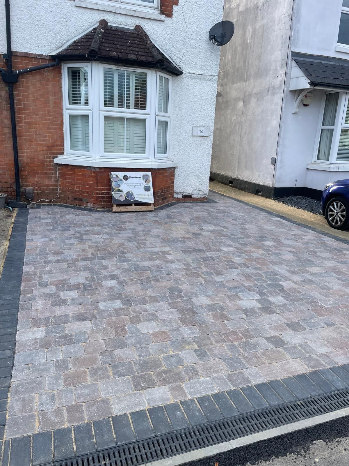 Stone-paved driveway beside a white and red brick house with bay windows and a parked car
