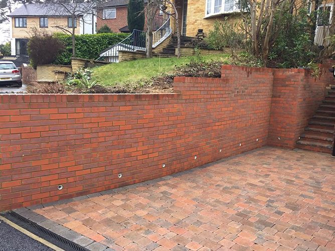 A brick wall surrounds a driveway with stairs leading up to a house.