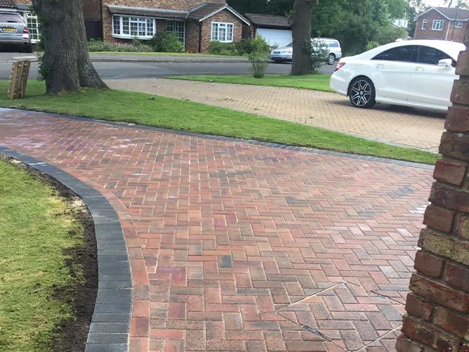 A white car is parked in a driveway next to a brick driveway.