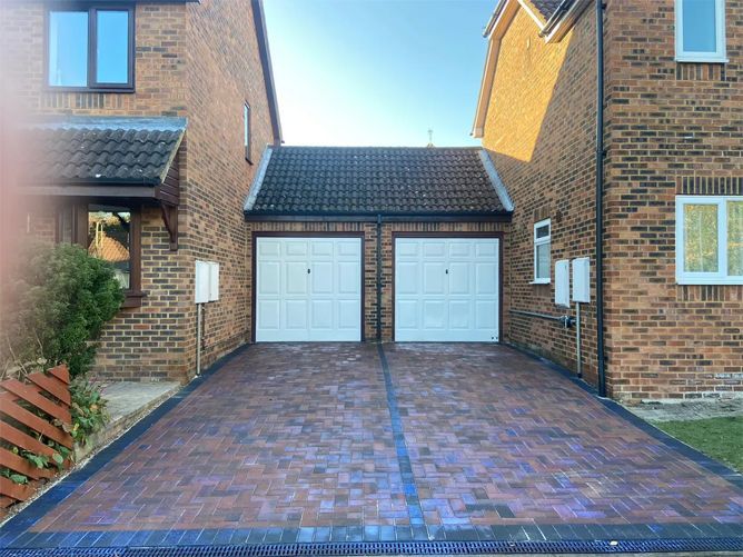 A driveway leading to a brick house with two garage doors.