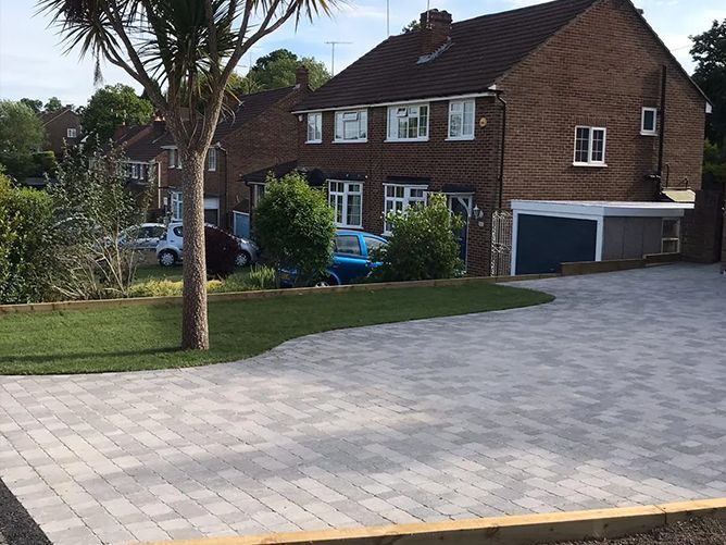 A driveway leading to a brick house with a blue car parked in front of it.