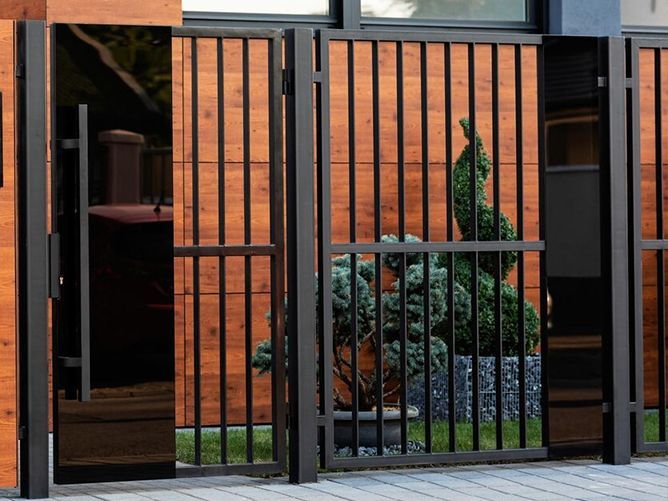 A black metal fence with a wooden wall behind it.