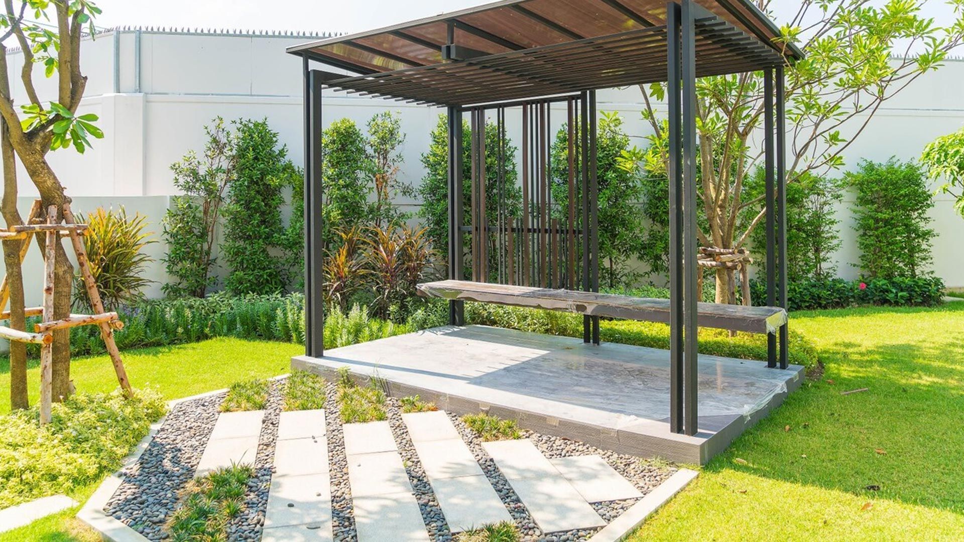 Modern backyard pergola with wood slatted roof, stone patio, and green lawn in bright sunlight