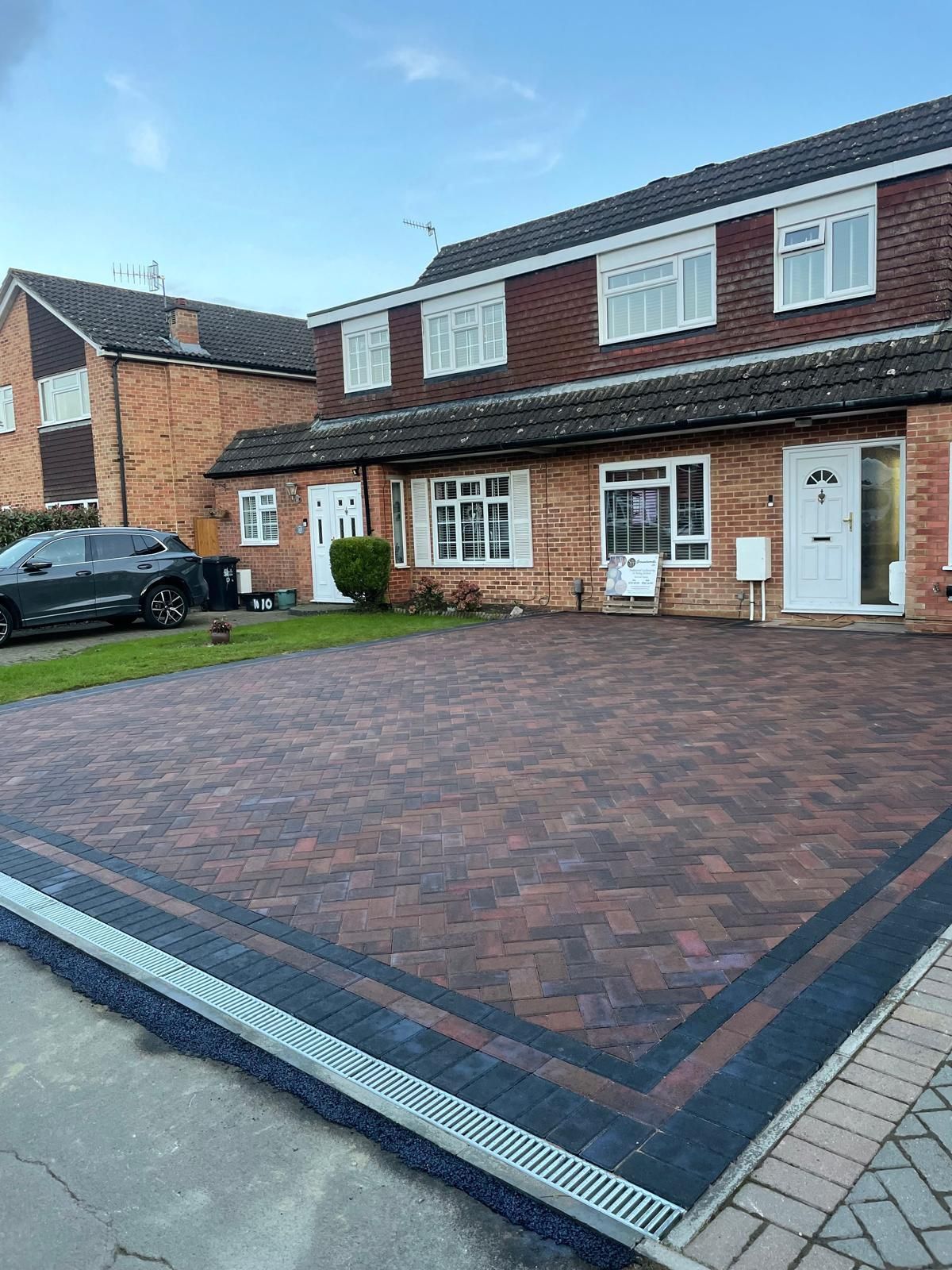Brick driveway in front of a brick townhouse with a black border and gutter along the edge.