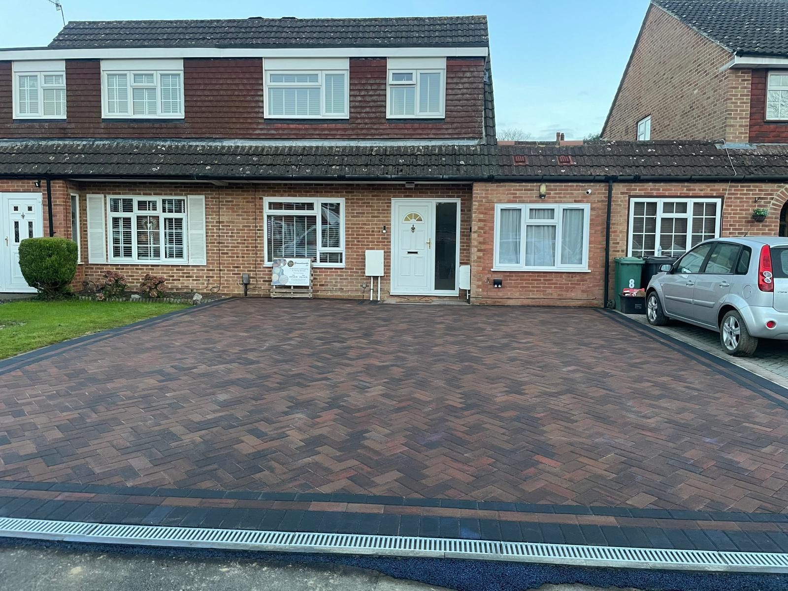 A car is parked in front of a brick house with a driveway.