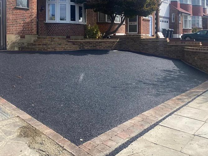 A tarmac driveway in front of a brick house.