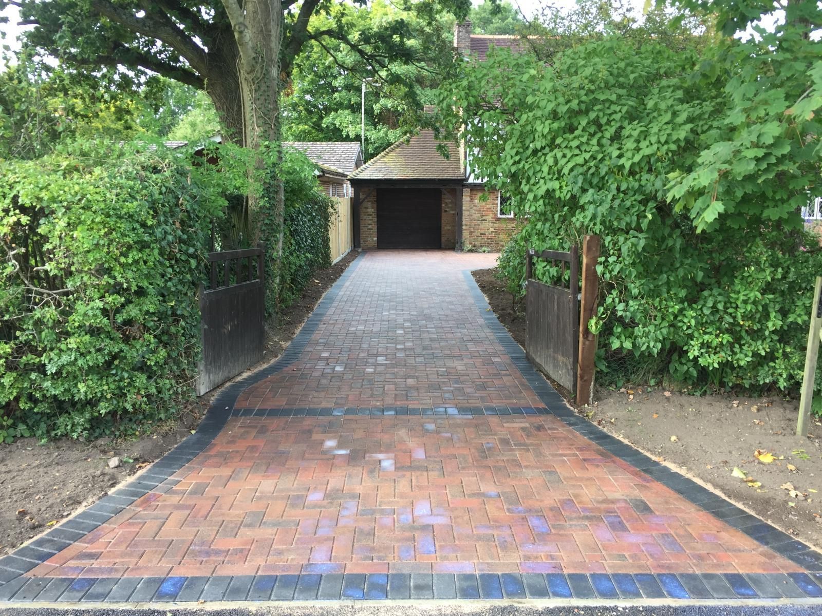 A brick driveway leading to a house surrounded by trees and bushes.