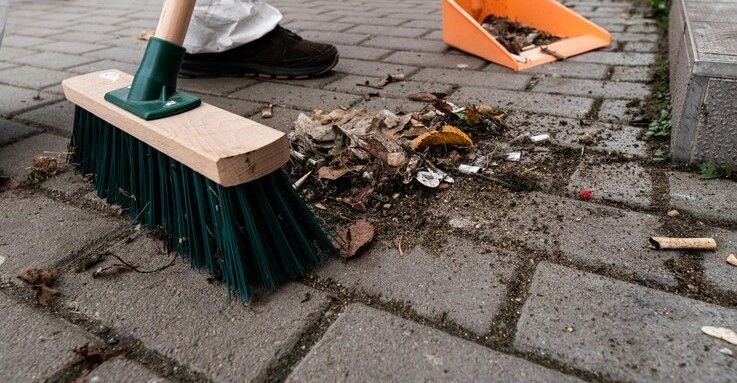 Person sweeping debris into a dustpan on a brick surface.