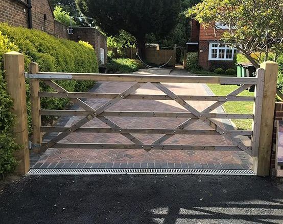 A wooden gate is open to a driveway in front of a house.