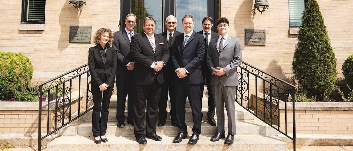 Five people in business attire stand on steps outside a brick building, posing for a group photo.