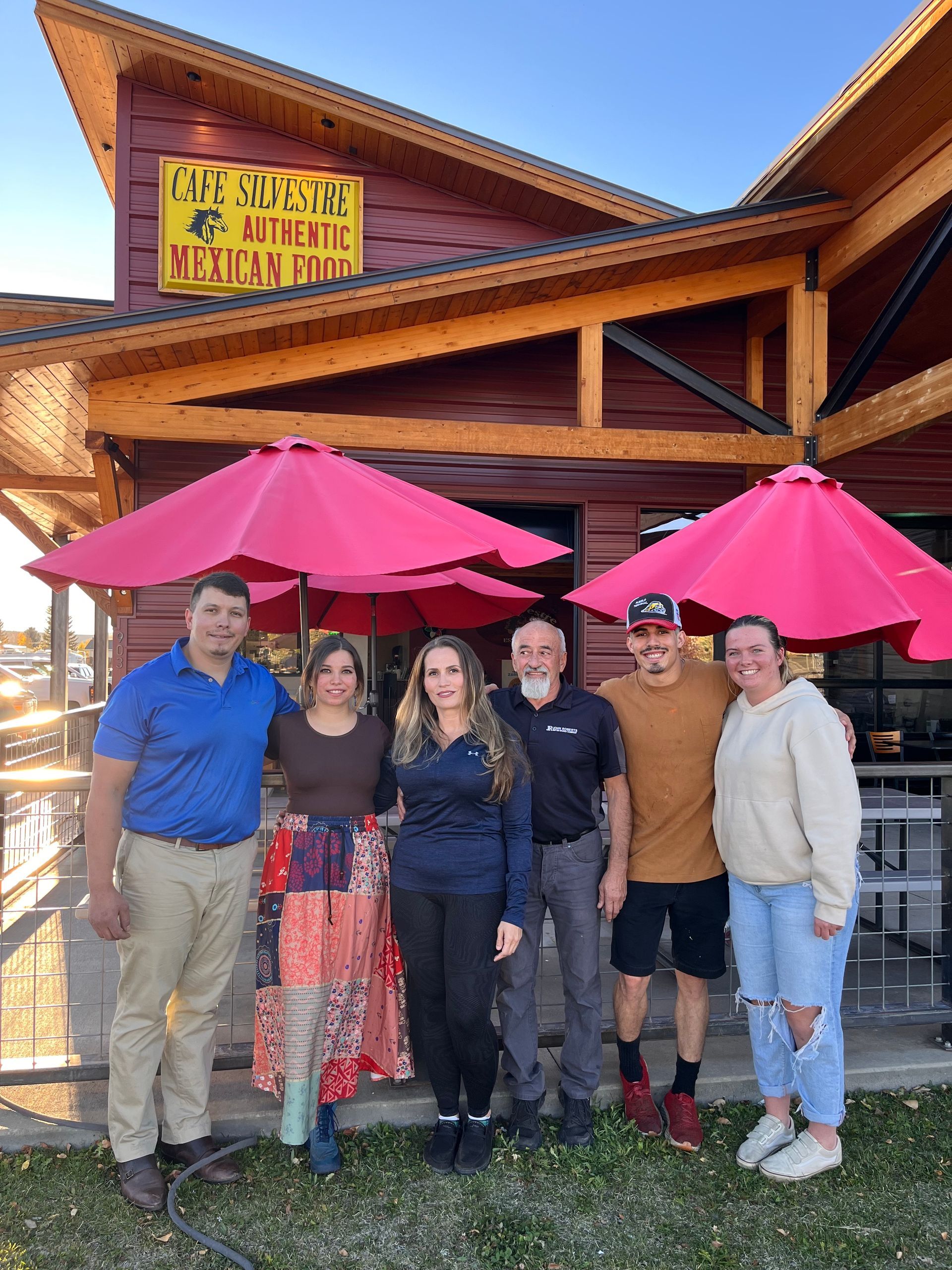A group of people are posing for a picture in front of a restaurant with pink umbrellas.