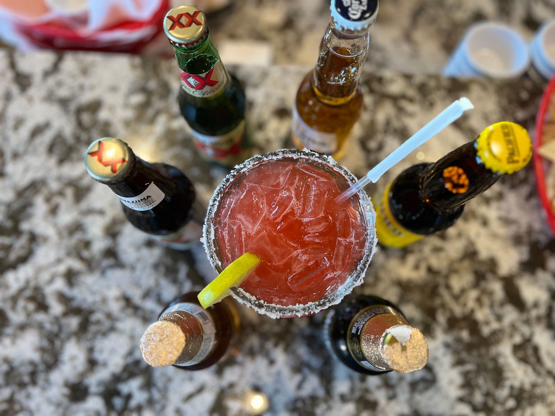 A margarita is surrounded by bottles of beer on a table.