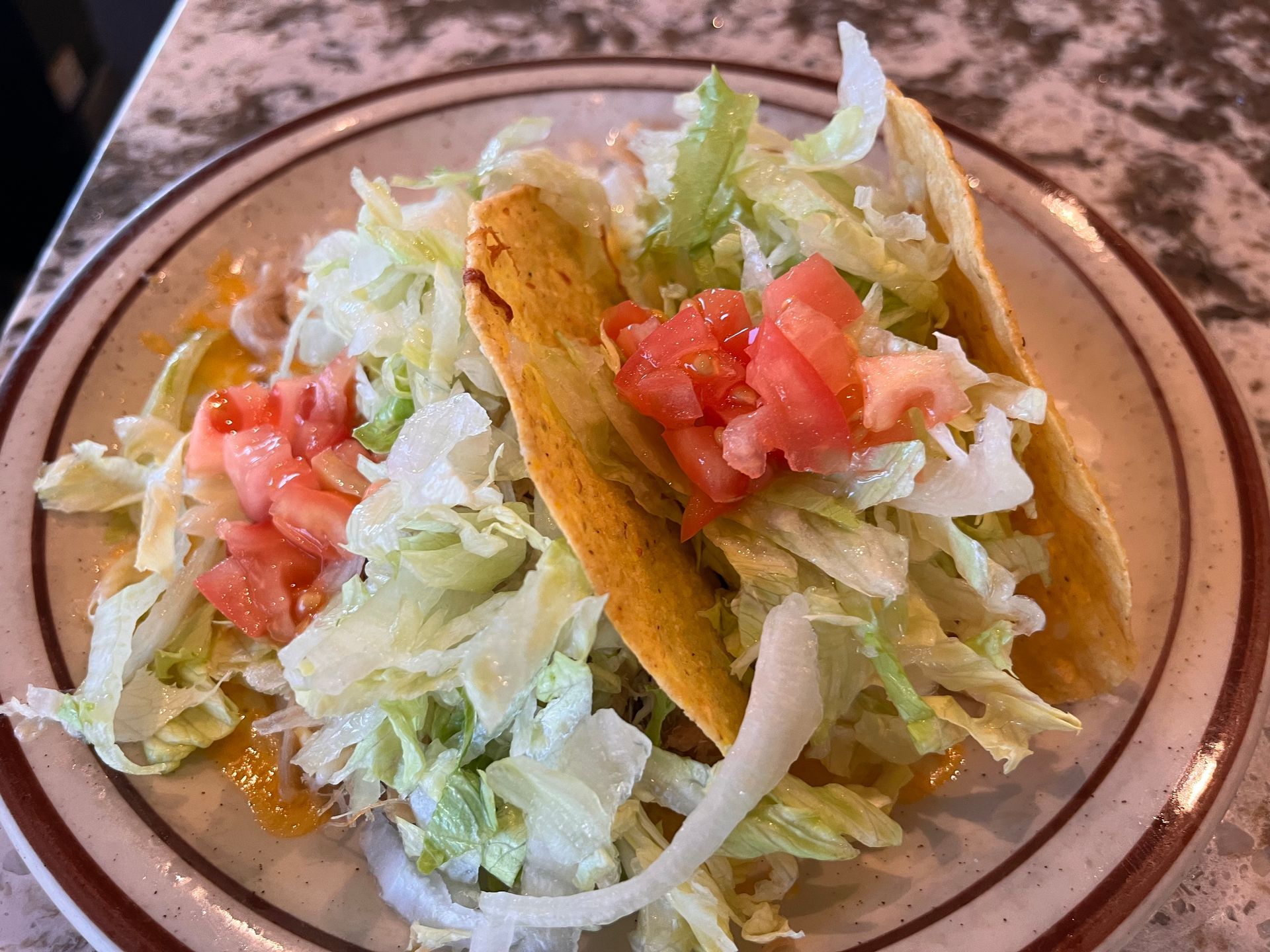 A plate of tacos with lettuce , tomatoes and cheese on a table.