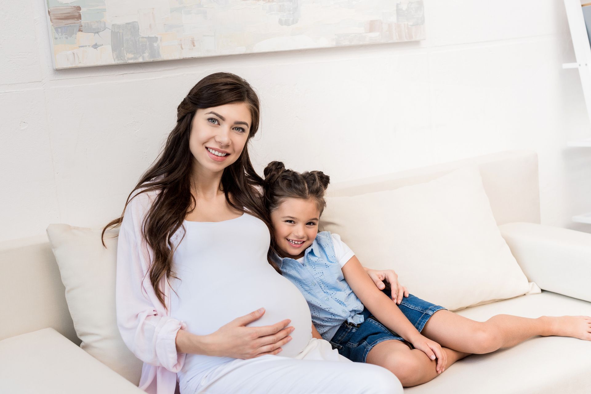 Pregnant woman and child on a couch, smiling at the camera.