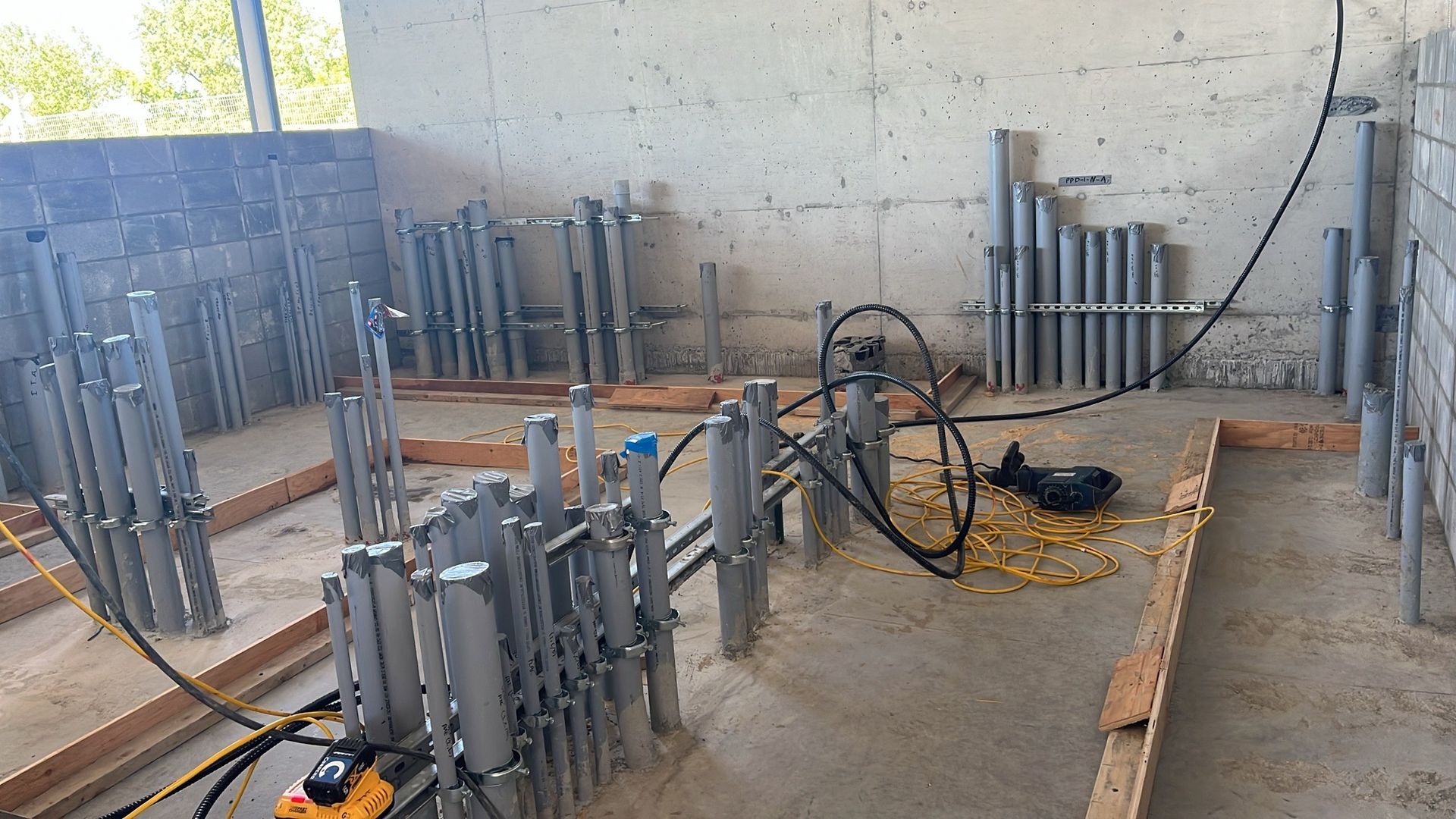 A room with a lot of pipes and a drill on the floor.