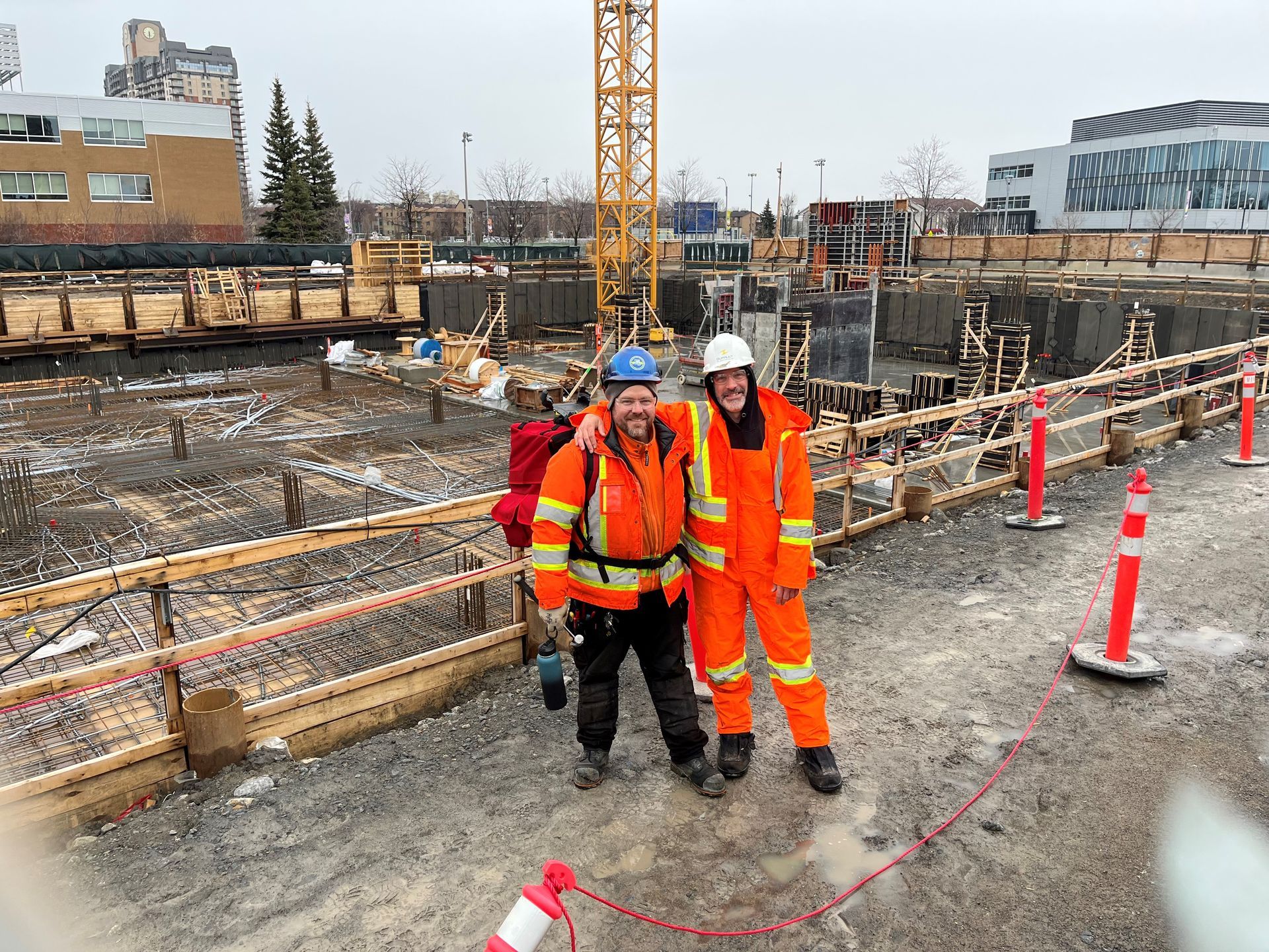 Two construction workers are posing for a picture at a construction site.
