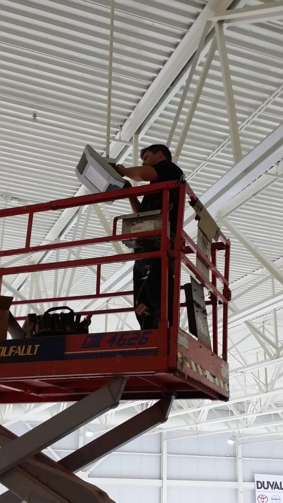A man is standing on a scissor lift working on a light fixture.