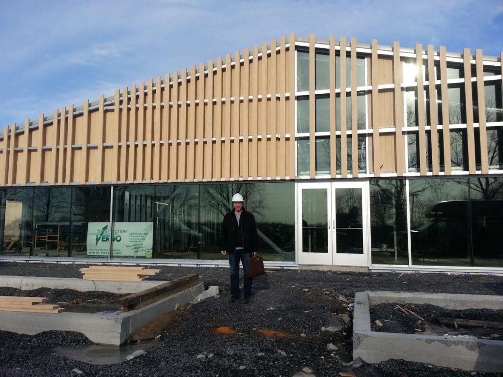 A man in a hard hat stands in front of a building under construction