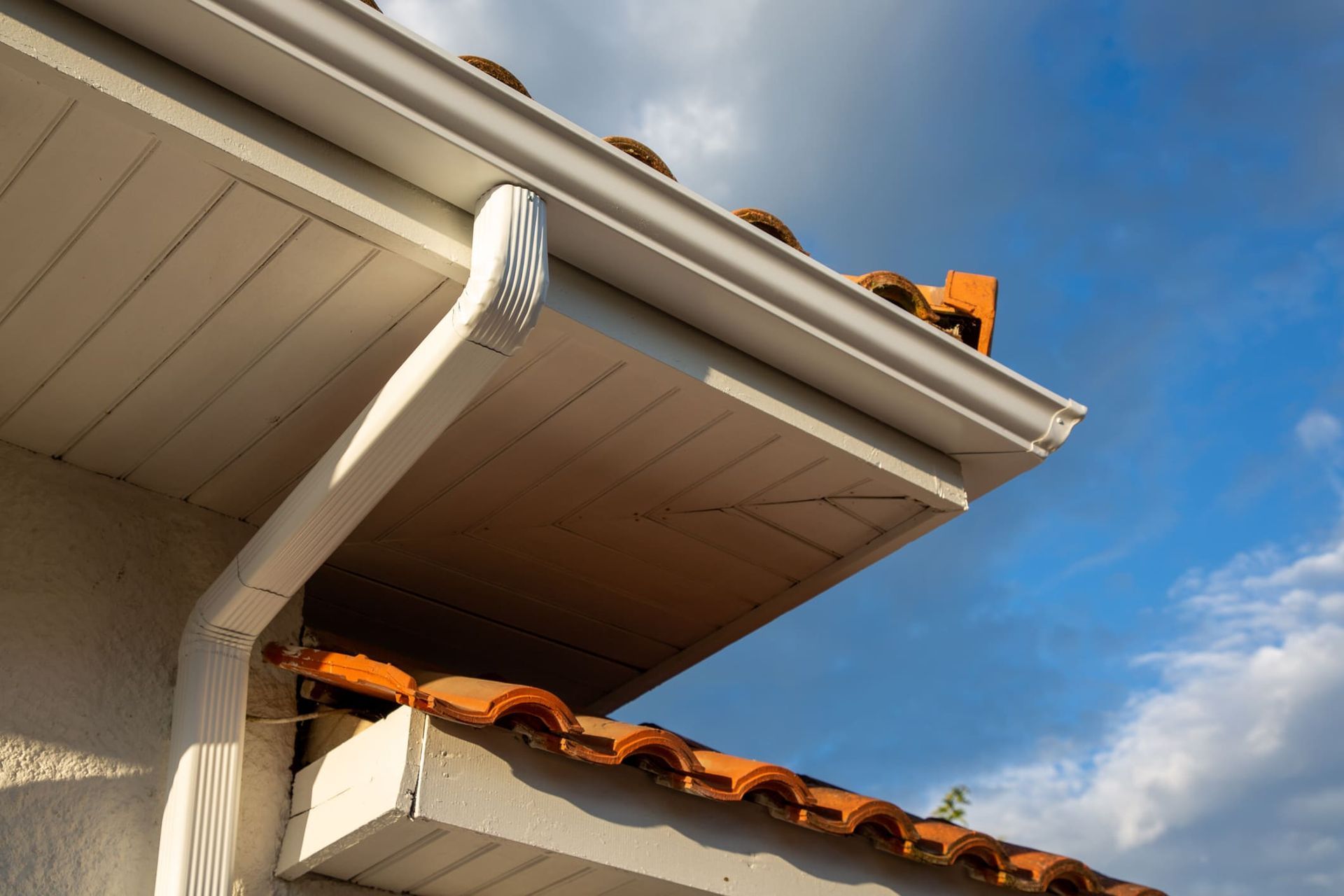 A white gutter on the side of a house with a tiled roof.