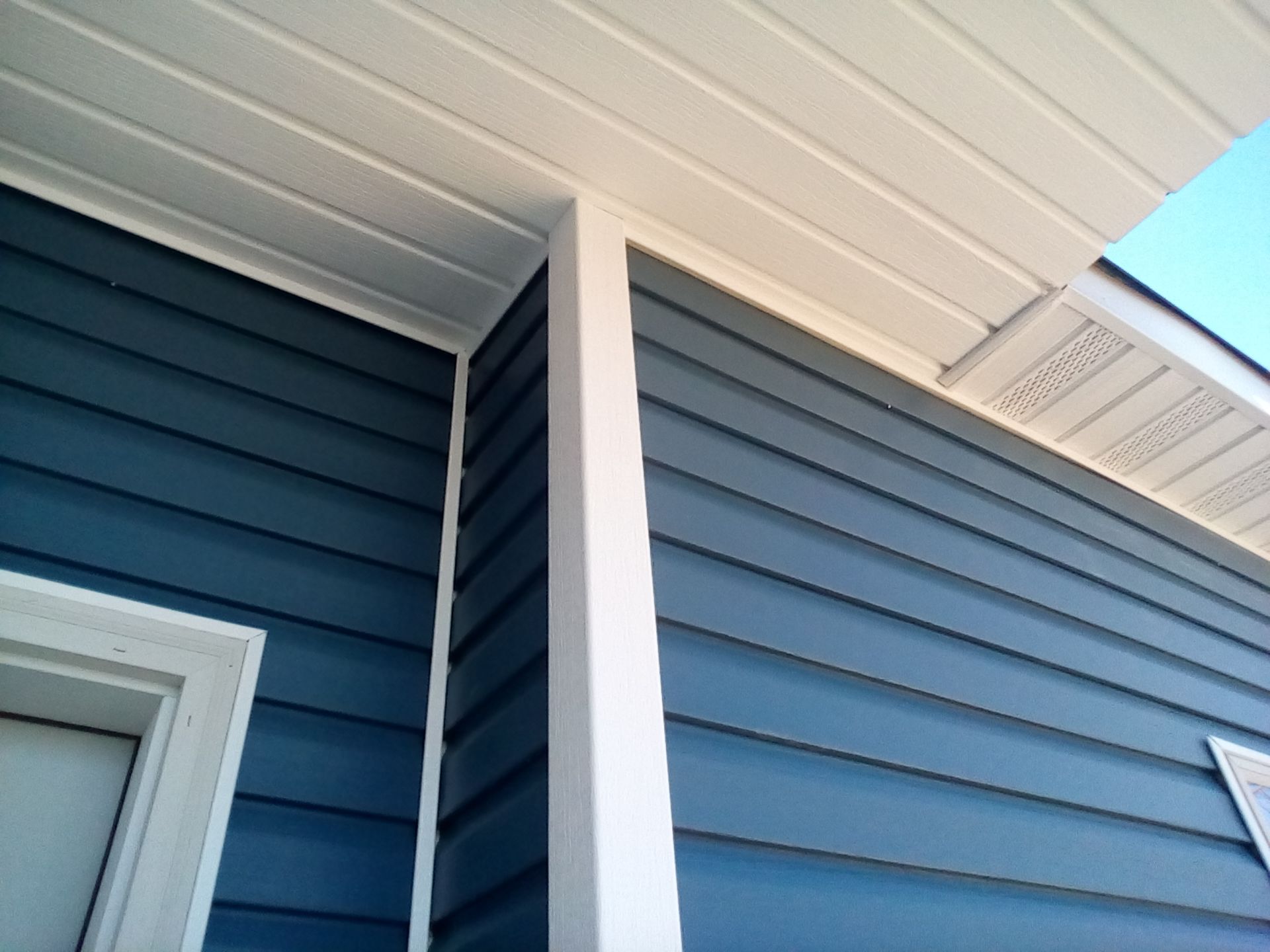 Corner of a blue house with white trim and soffit under a porch roof, viewed from below