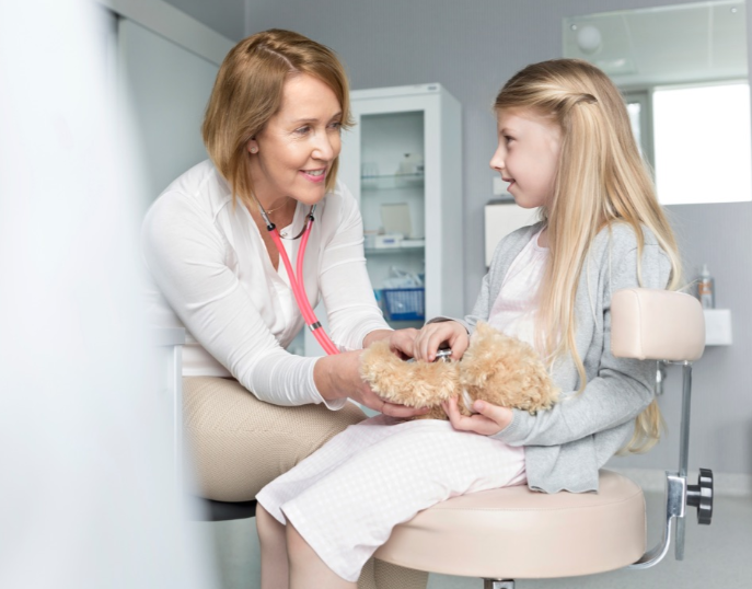 A doctor uses her stethoscope to check the heartrate of a child's teddy bear.
