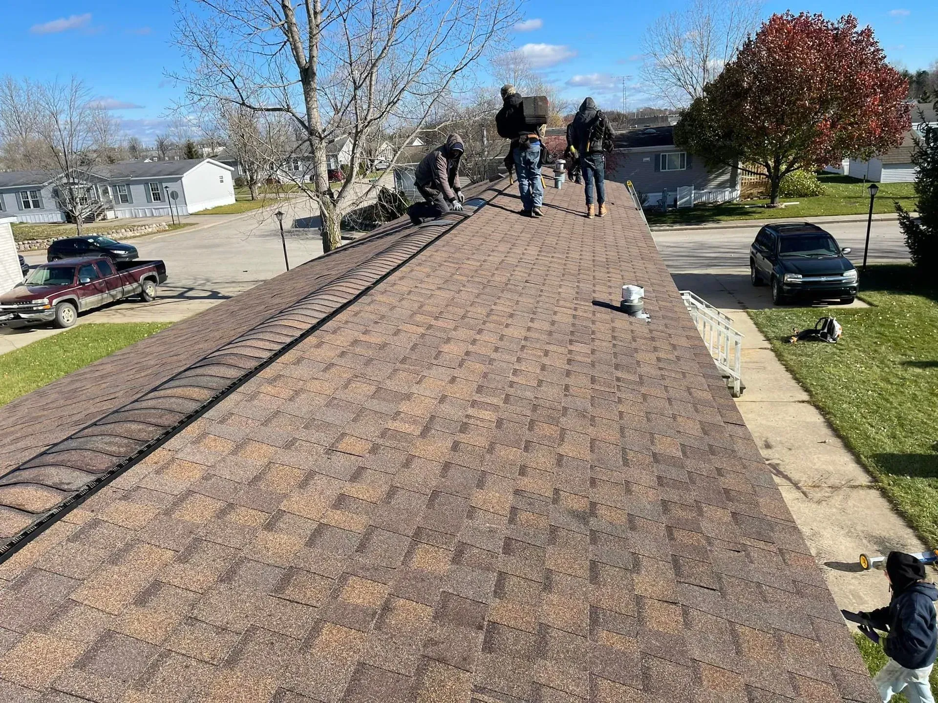Workers installing brown shingles on a house roof in a suburban neighborhood