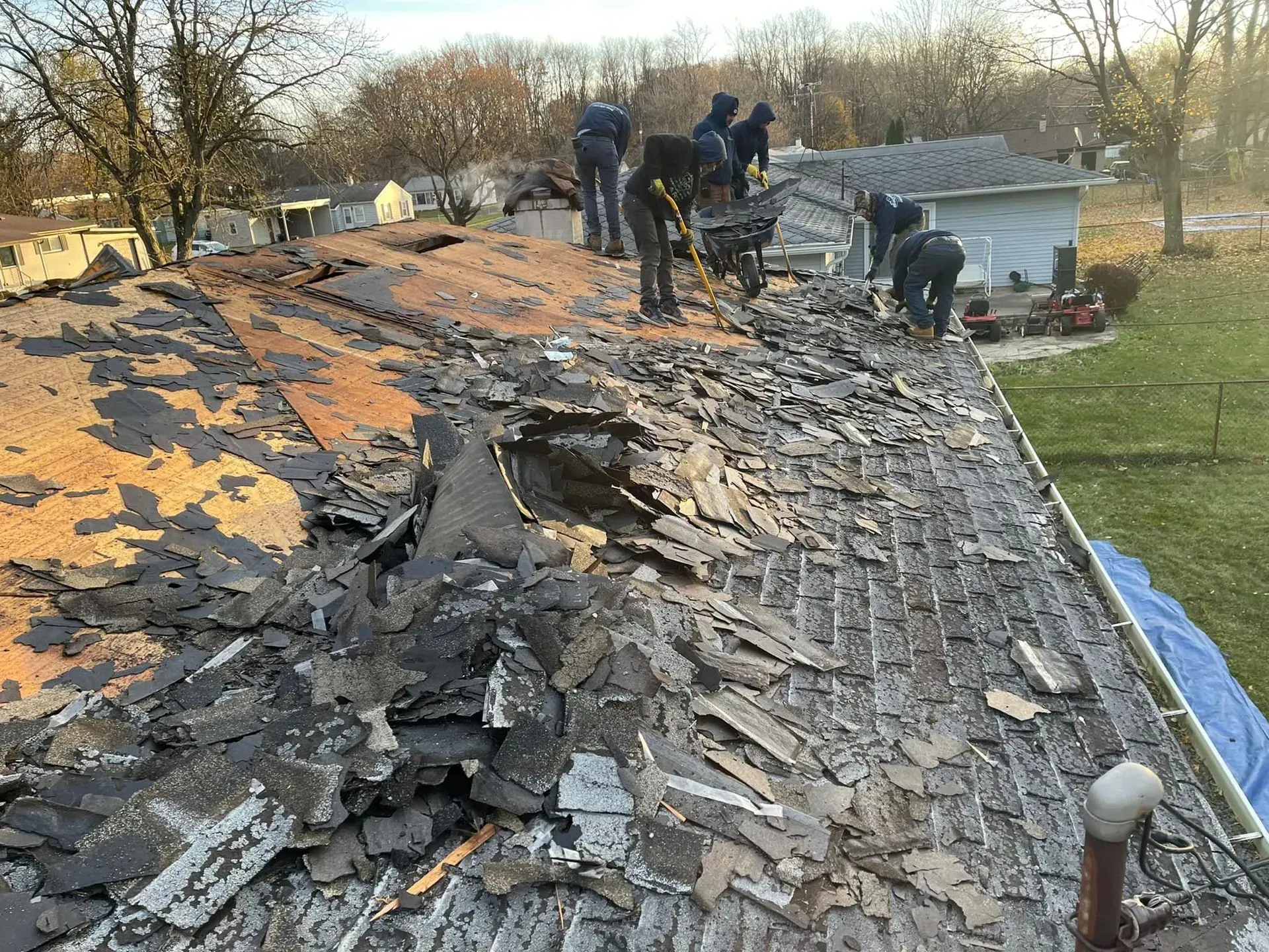 Workers repairing a damaged shingled roof with exposed tar paper and debris.