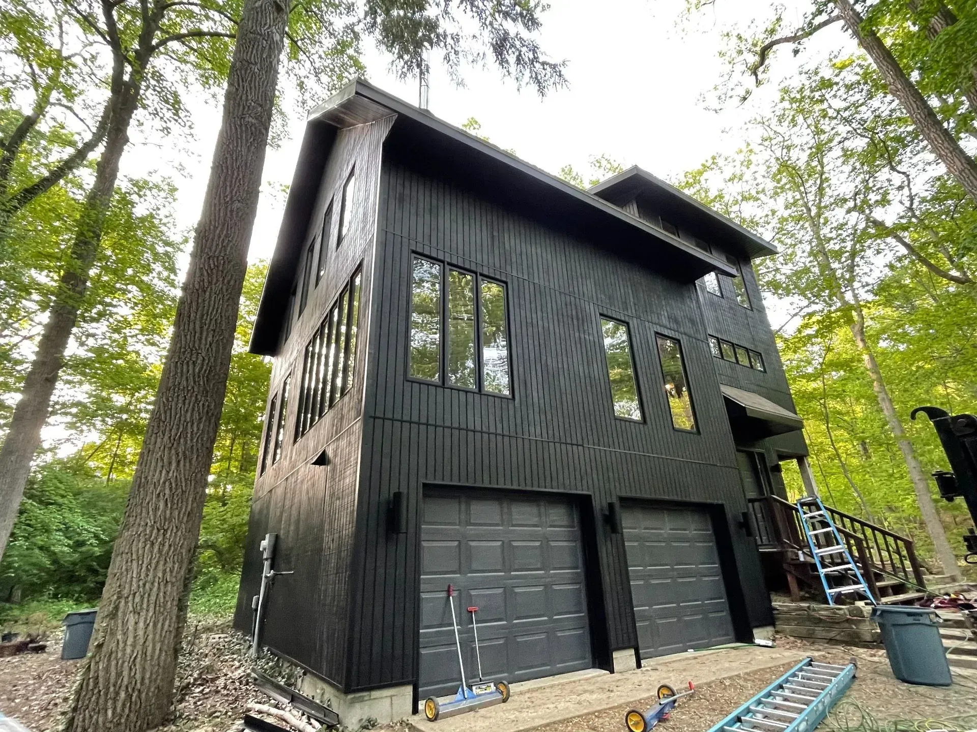 Black modern two-story house with garage and tall windows in a wooded setting