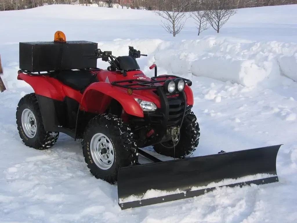 Red ATV with front snowplow in snowy field