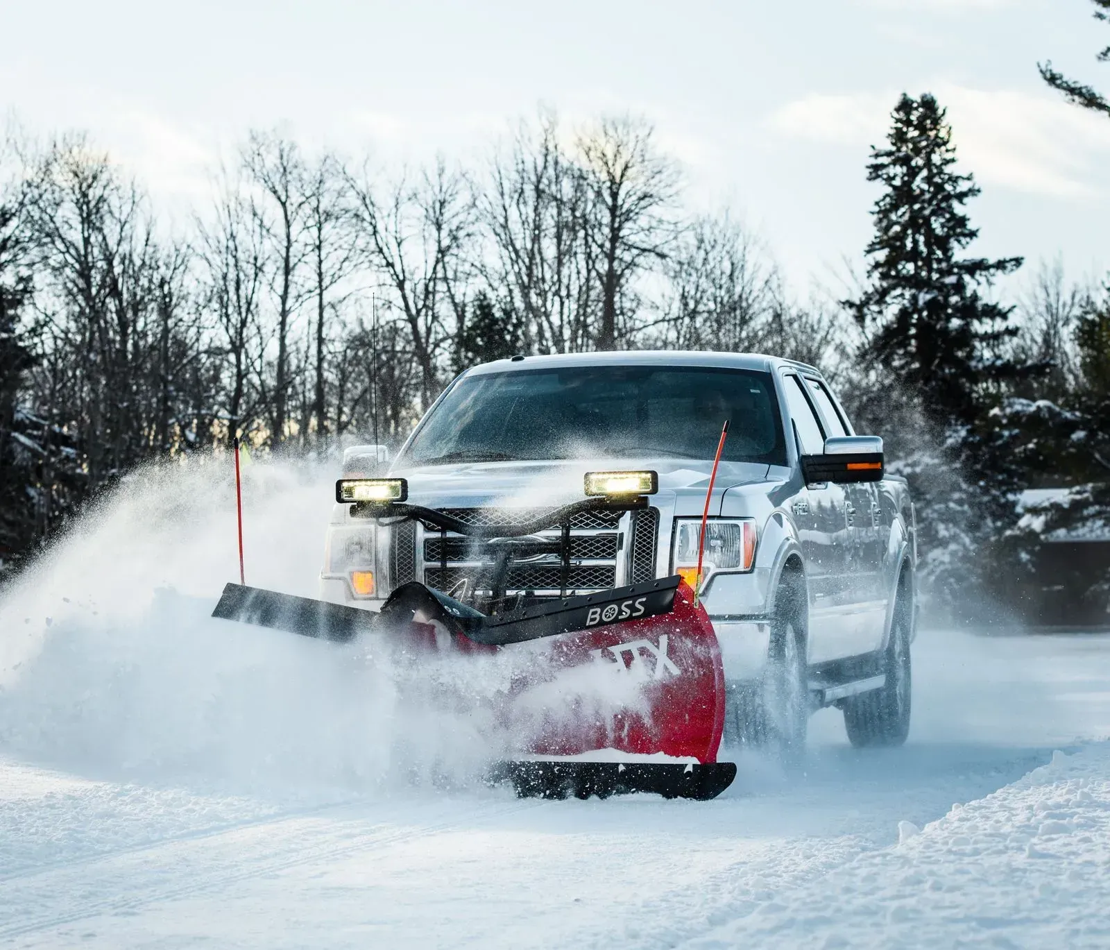 Pickup truck with red snowplow clearing a snowy road in winter