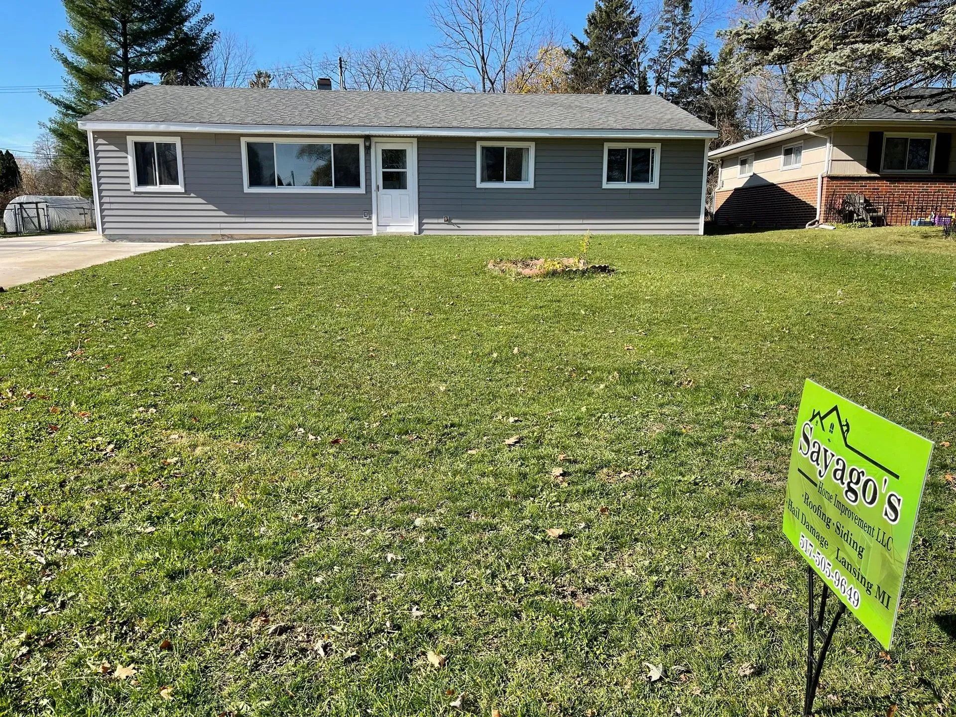 Single-story gray house with a large front lawn and a green for-sale sign in the yard.