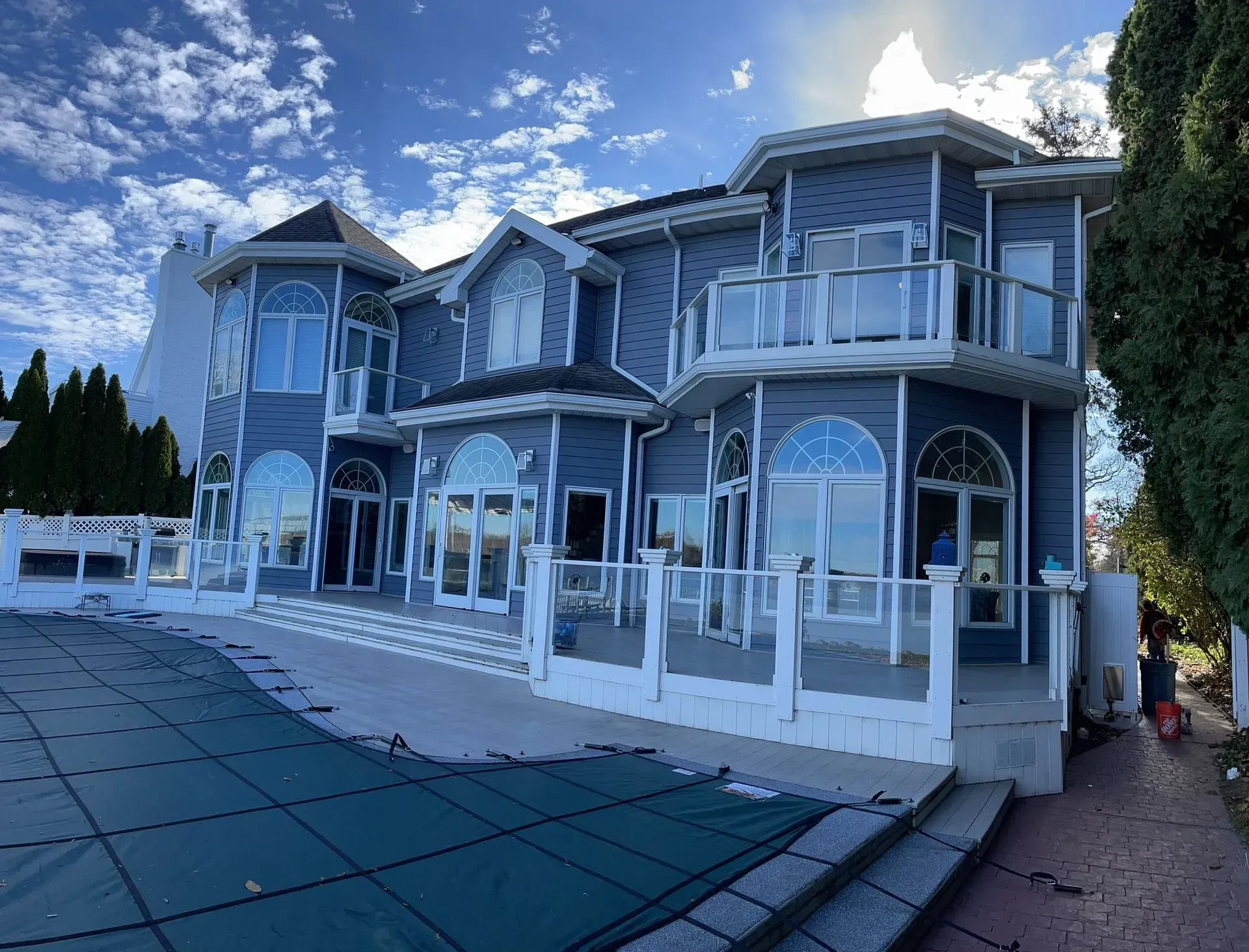 Large blue-gray Victorian-style house with a glass-enclosed patio and white railings beside a pool cover