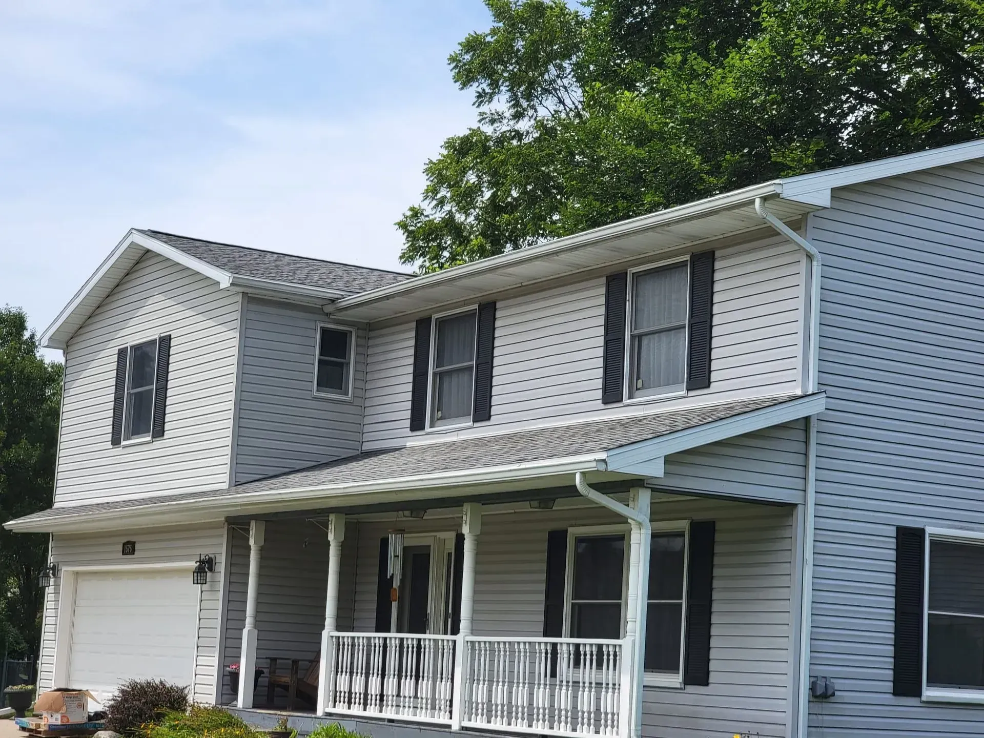 Two-story white house with gray siding, black shutters, and a front porch under leafy trees
