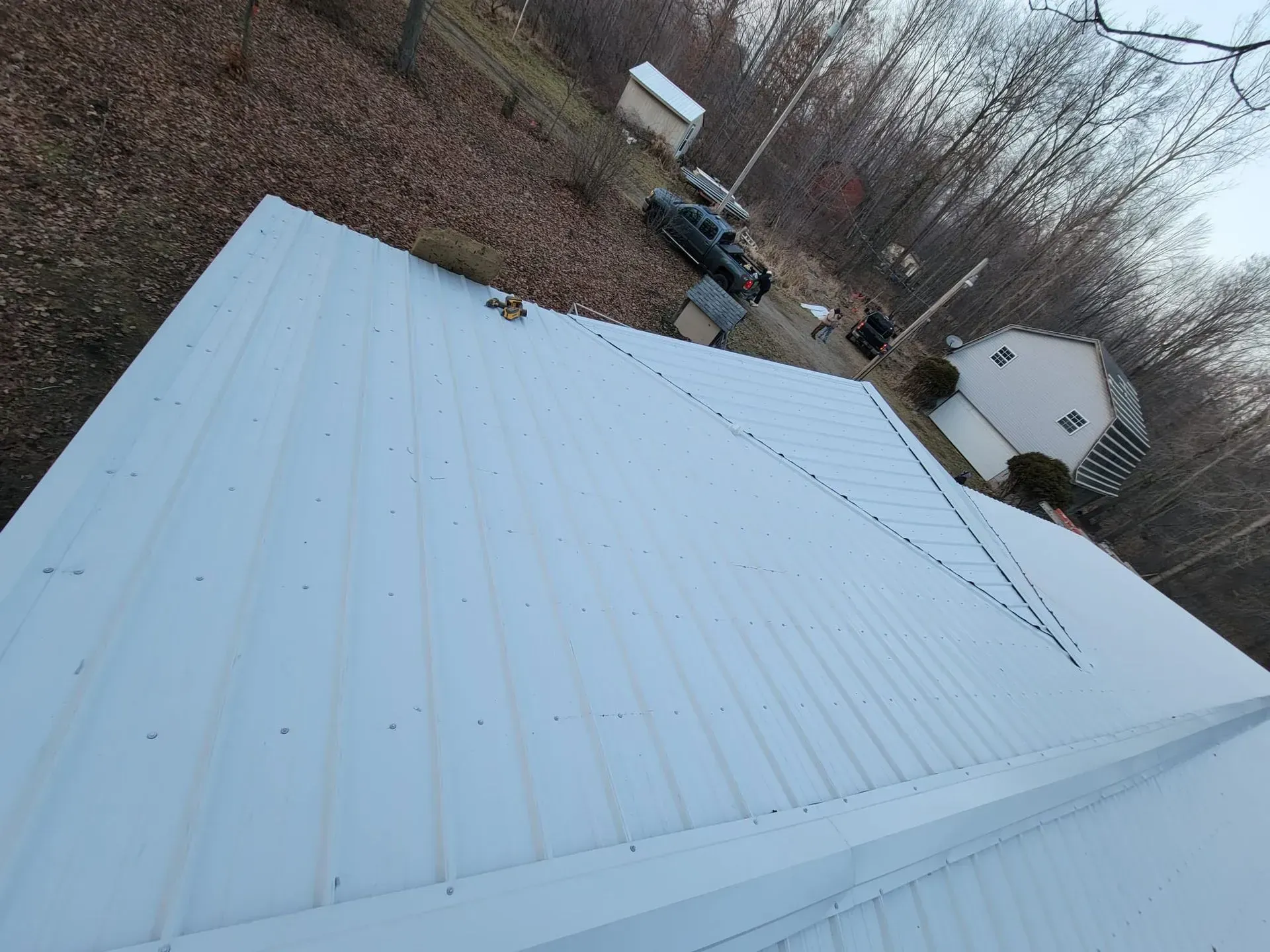 Snow-covered white roof with a steep pitch, seen from above with trees and a parked vehicle nearby.