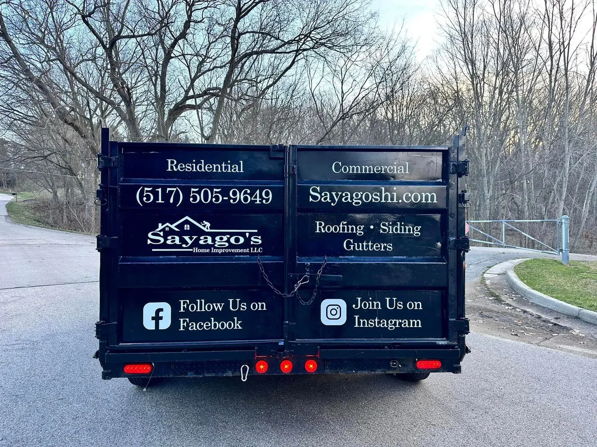 Back of black contractor van with Savagoos roofing and siding signage on a roadside curve