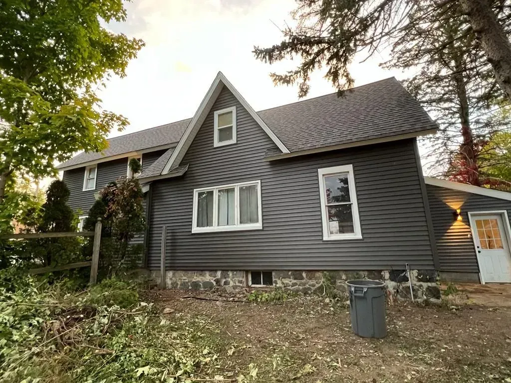 Gray house with steep roof and white trim, seen from a yard with trees and fallen leaves