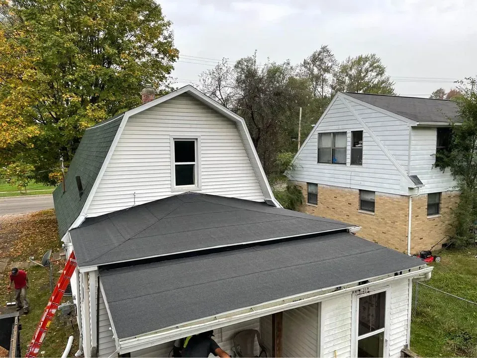 Damaged house roof and awning with a white siding home in the background