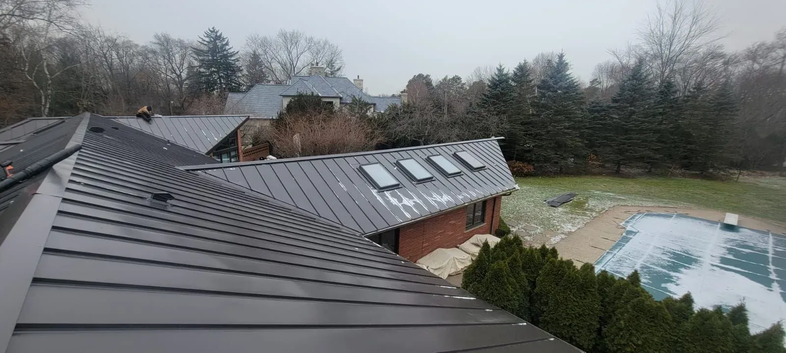 Rooftop view of a house, with a backyard pool and leafless trees on a cloudy day