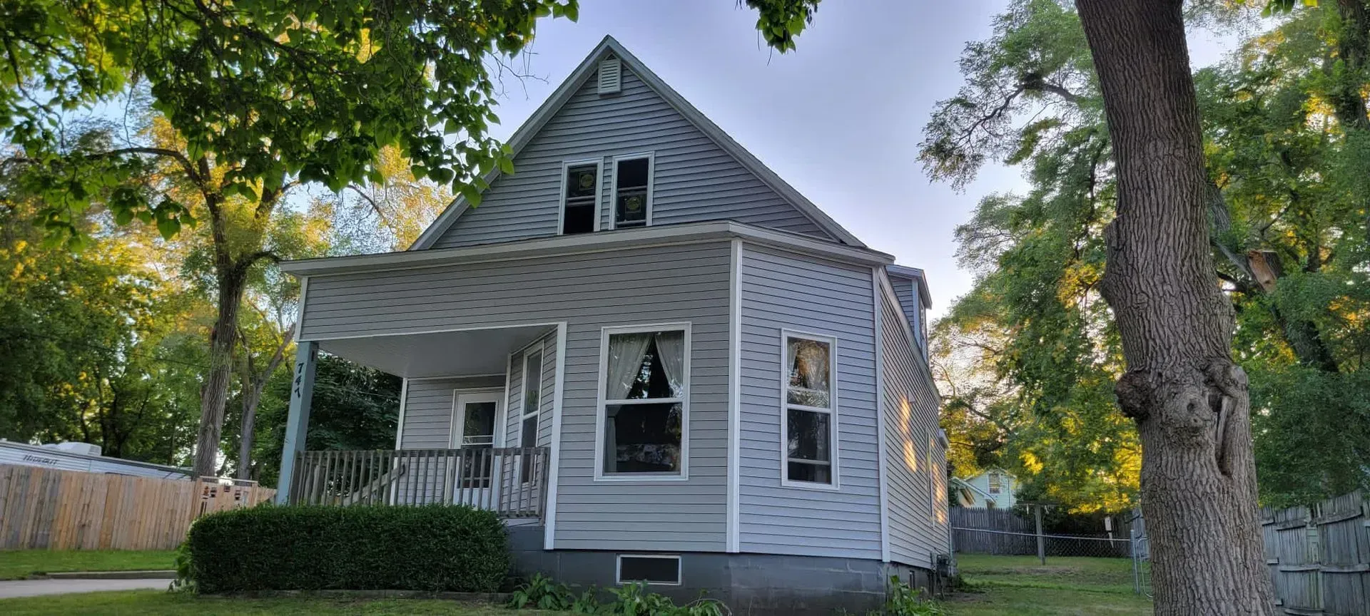 Gray house with white porch and trim, surrounded by trees on a sunny day