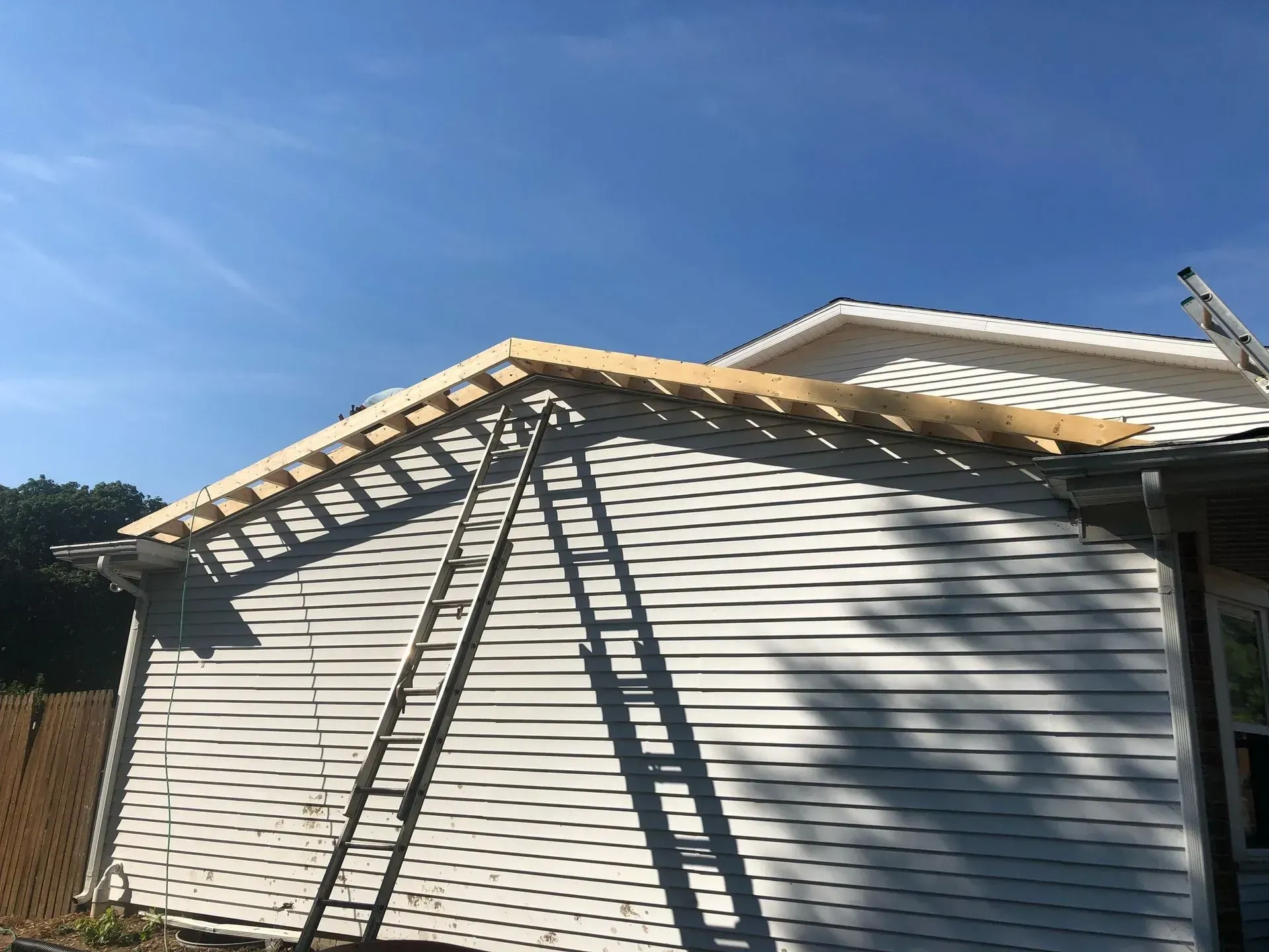 Backyard house exterior with white siding, blue sky, and ladders leaning against the wall